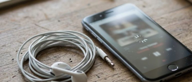 Смартфон с проигрывателем музыки и наушники на деревянном столе